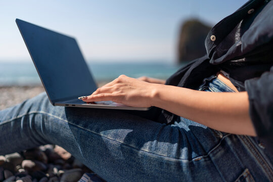 Laptop typing freelancer woman working remotely on beach vacation by the ocean