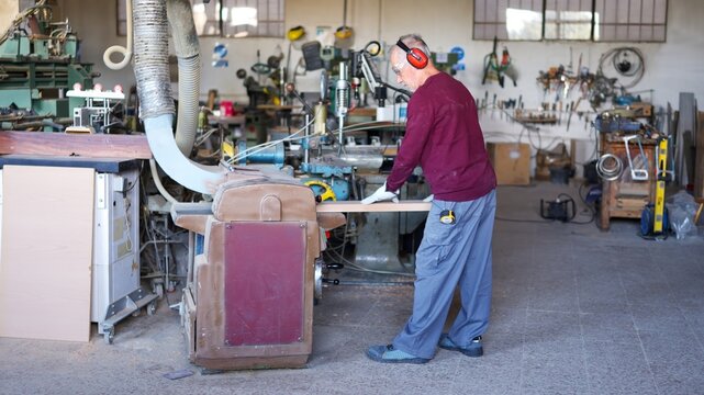 Elderly man working wood plank with a thicknesser in workshop