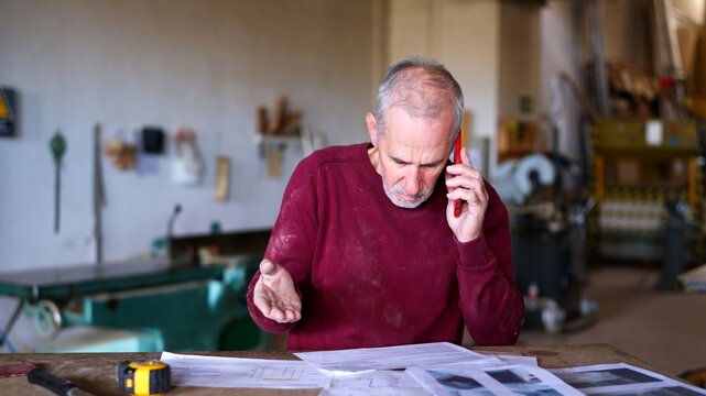 Senior craftsman receiving phone call managing workshop business