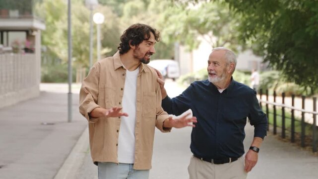 Adult son and senior father walking together smiling and talking in park showing friendship bond