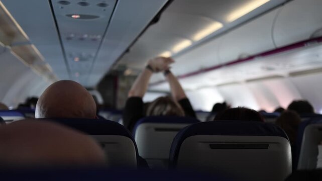 Passengers inside airplane cabin during flight person raising hand toward overhead panel seats rows perspective travel aviation interior in air journey atmosphere