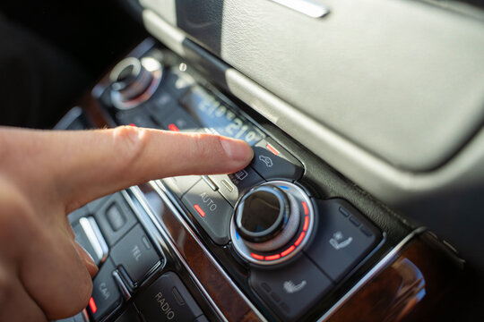 Finger presses air recirculation button on car climate control panel, adjusting airflow mode in vehicle interior with dual zone temperature display.