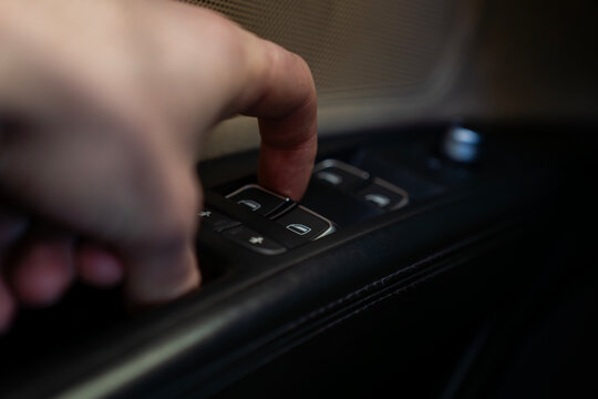 Hand pressing power window switch on car door panel, close up of control buttons and speaker grille, automotive interior detail.
