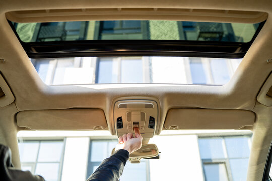 Driver hand pressing sunroof control button on overhead console, operating panoramic roof opening system inside car