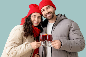 Beautiful young couple in warm clothes with glass cups of hot mulled wine on turquoise background