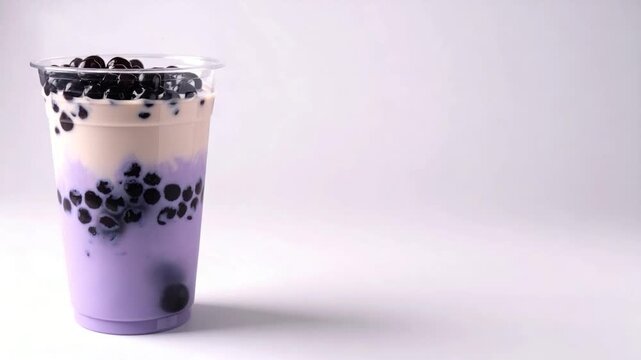 A tall transparent cup holds layered purple-hued drink with dark, round, bobbling spheres