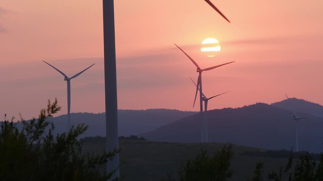 Windmills stand tall in evening light and produce energy. Blades of wind turbines move constantly to produce renewable electricity