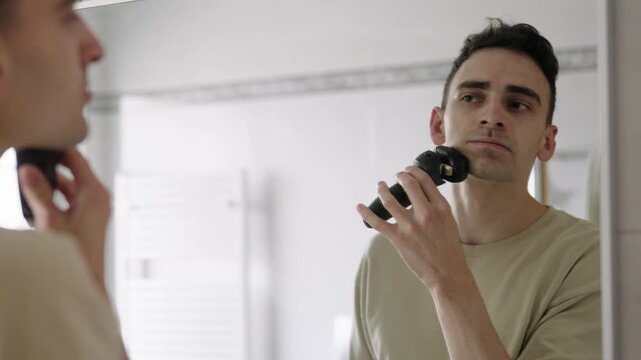 A man carefully shaves his beard in front of the bathroom mirror, part of his daily grooming and self-care routine.