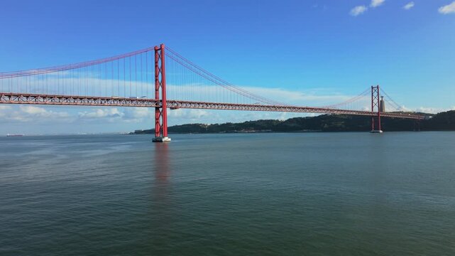 Aerial view of April Bridge. drone panorama de Abril bridge Lisbon calm Tejo river clear blue sky distant Cristo Rei silhouette midday light slow lateral reveal perfect for travel