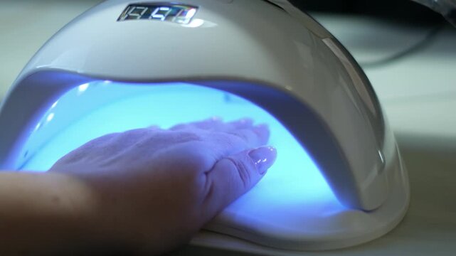 Brief video showing a hand being cured under a UV LED nail lamp for a gel manicure. High quality 4k footage
