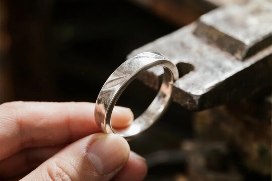 Hand holding a handmade silver ring with textured surface near a metal workbench