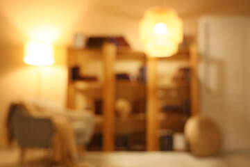 Blurred view of stylish living room with grey armchair, glowing lamps and bookshelves at evening © Pixel-Shot