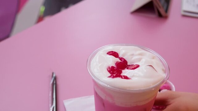 Hand adds cherry atop whipped cream, chocolate syrup, and sprinkles on pink strawberry milkshake
