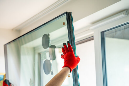 Worker installing new triple glazed window glass unit into frame in apartment interior. Window replacement, home improvement and professional installation process concept.