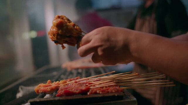 The chef puts skewers with satay meat on the grill. Street food in Asia is delicious cuisine at local markets.