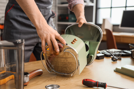 Male worker repairing coffee machine at table in workshop, closeup