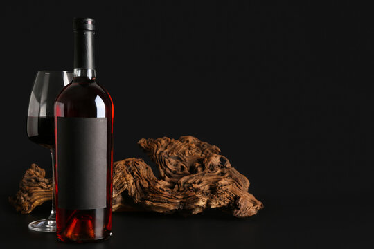 Bottle and glass of red wine with wood on black background