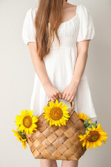 Naklejka premium Young woman with beautiful sunflowers in wicker basket on light background