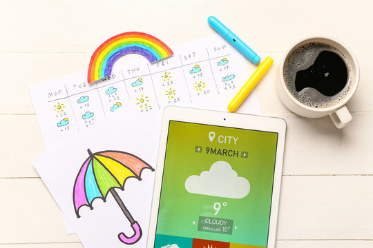Tablet computer with weather forecast, drawn umbrella and cup of coffee on white wooden background