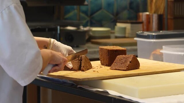 Professional Baker Slicing Dark Rye Bread with Seeds. Chef slicing a triangular loaf of dark coriander rye bread on a wooden board. Professional kitchen setting for bakery, restaurant