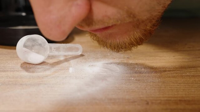 Scattered White Powder on a Wooden Table, Man Licking It Off, Close-Up. Measuring Spoon Lying Nearby.