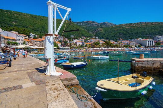 Scenic view of Petrovac harbor in Montenegro with traditional fishing boats moored in turquoise Adriatic sea under blue summer sky.