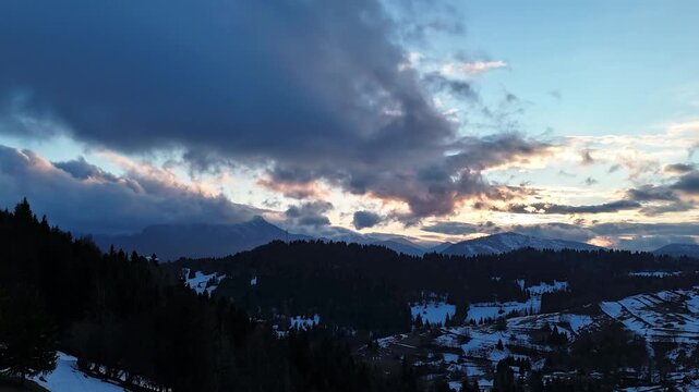 Forward flying aerial hyperlapse over snowy rural landscape during sunset with dramatic clouds