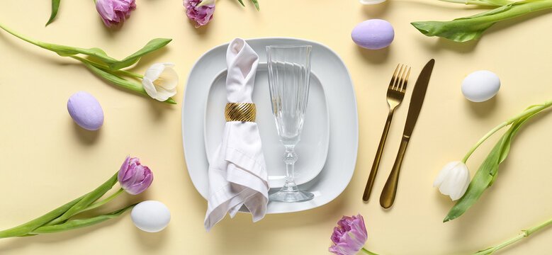 Table setting with Easter eggs and beautiful tulips on yellow background