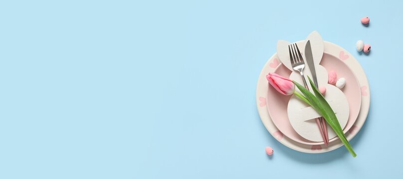 Easter table setting with paper bunny, eggs and tulip flower on light blue background with space for text