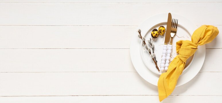 Beautiful table setting with napkin, quail eggs and pussy willow branches on white wooden background with space for text