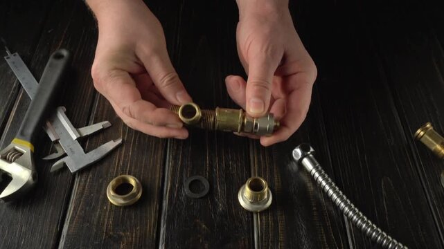 Hands of master connecting brass plumbing fittings on a wooden workbench, with various tools and components arranged around, illustrating the assembly process in a workshop setting