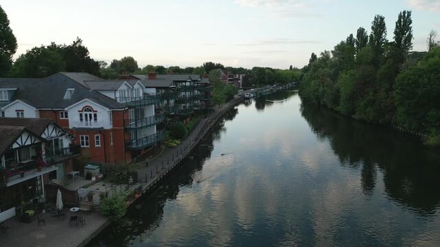 Riverfront homes and trees line a calm river with reflections of the sky.