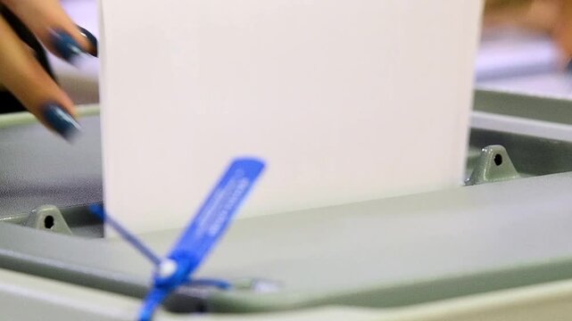 Close-up of a man's hands dropping sheets of paper or a ballot into a voting machine.
