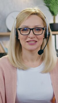 Portrait of charming confident successful joyful light-haired businesswoman in wireless headset which posing on camera at her workplace in beautifully decorated room,slow motion