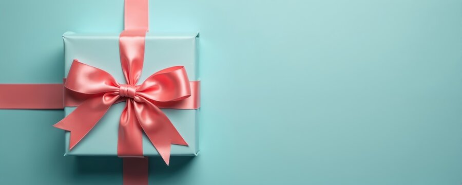 Light blue gift box with coral pink ribbon bow on matching background. Perfect for celebrations, sales, and special offers. Presents for holidays or birthdays.