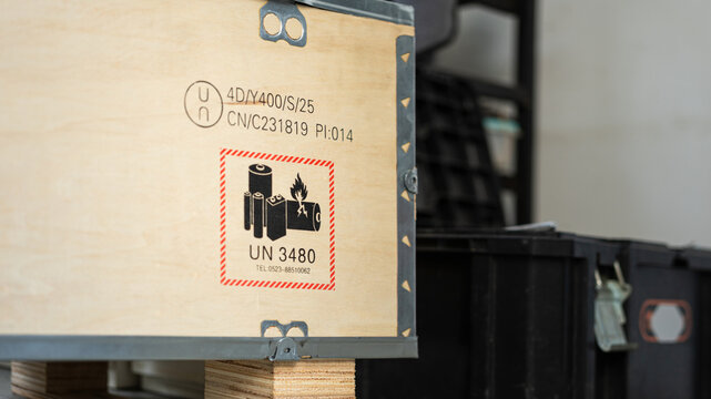 Safety label and placard of high voltage battery or electronic component equipment in the wooden crate, safety sign for dangerous good transportation. Close-up with selective focus.