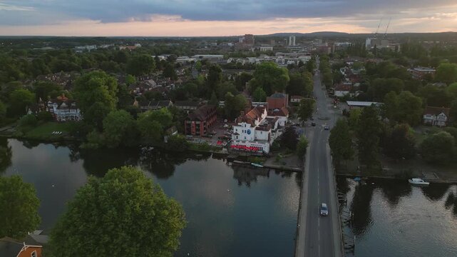 A scenic aerial view captures a town nestled beside a river at dusk. Buildings, trees, and a bridge with cars hint at a peaceful evening.