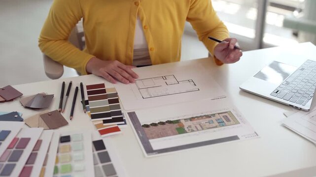 Asian adult designer architect selecting material samples drawing floor plan working new project developing design scheme professional studio workspace creative process