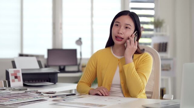 Asian adult woman designer professional talking phone call home office discussing creative project business communication client collaboration remote work productivity