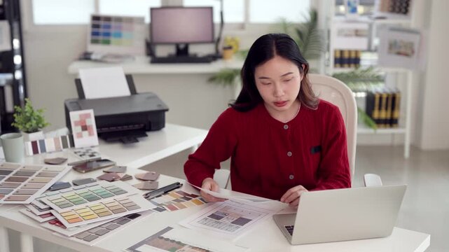 Asian adult woman designer reviewing project documents creating color palettes office workspace professional interior architecture planning development