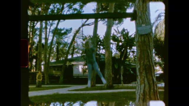 A child in a blue outfit is captured swinging on a simple rope swing in a backyard on super 8 film