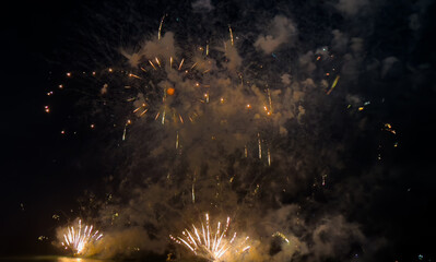 Naklejka premium Vibrant fireworks burst in the night sky, illuminating a grand building and its colorful reflections on the calm water below.