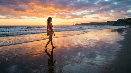 Fototapeta premium A young woman walks barefoot along a pristine beach at sunset, her reflection mirroring the vibrant, colorful sky and ocean waves during the golden hour.