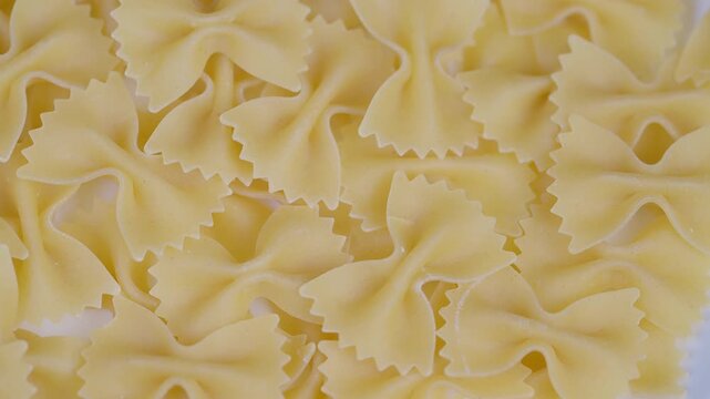 Uncooked bowtie pasta arrangement captured. Detailed view showing raw farfalle with textured surface. Snapshot capturing intricate design of uncooked farfalle pasta in detail