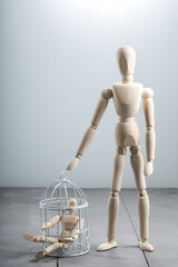Large wooden mannequin standing beside birdcage containing small figure, protection and care concept