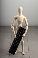 Wooden mannequin holding television remote control, control and modern convenience concept