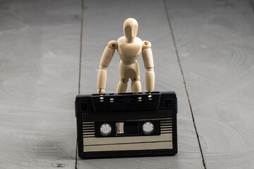 Wooden mannequin standing with audio cassette at feet, nostalgia and forgotten media concept
