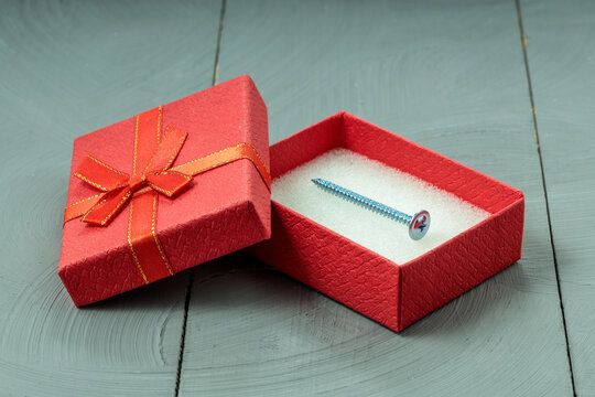 Zinc screw inside open red gift box on wooden surface.