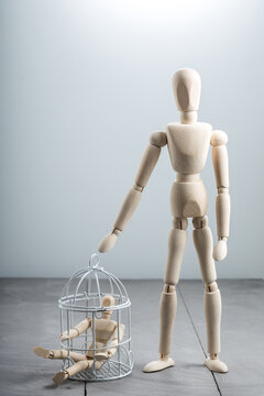 Large wooden mannequin standing beside birdcage containing small figure, protection and care concept