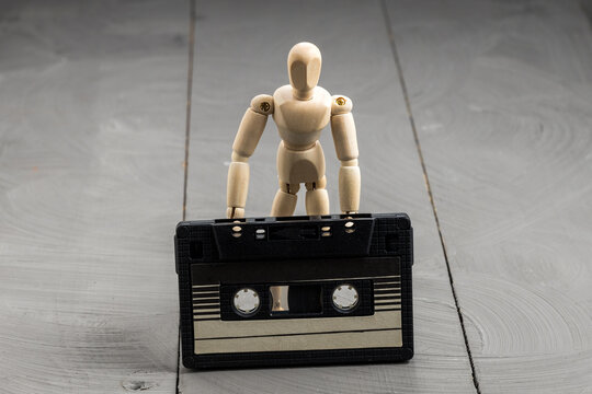 Wooden mannequin standing with audio cassette at feet, nostalgia and forgotten media concept